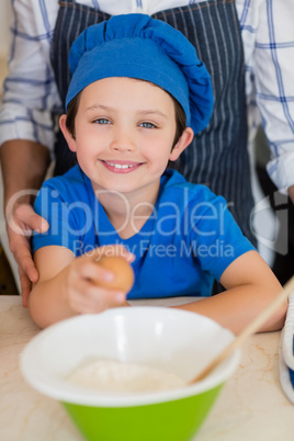 Smiling boy in chefs hat holding egg in kitchen