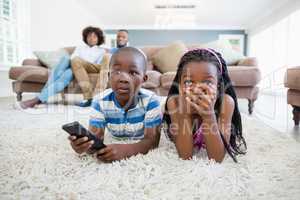 Siblings lying on rug and watching television in living room