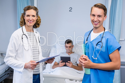 Doctors standing with reports and patient using digital tablet in background