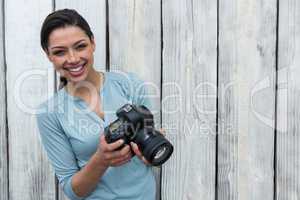 Happy female photographer standing against wooden background