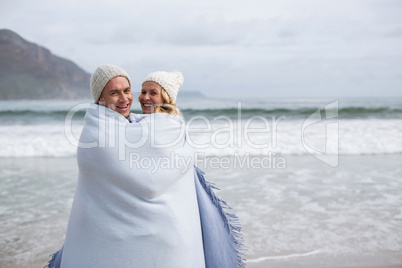 Mature couple wrapped in blanket on the beach