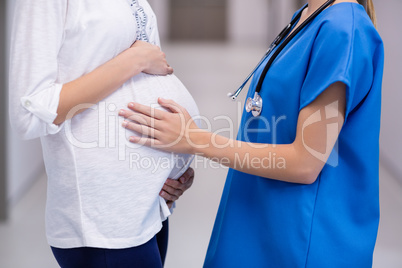 Mid section of doctor touching pregnant womans belly in corridor