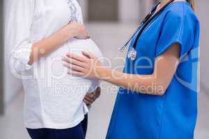 Mid section of doctor touching pregnant womans belly in corridor