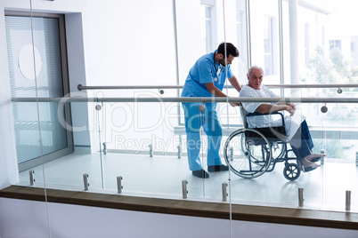 Male doctor pushing senior patient on wheelchair in passageway
