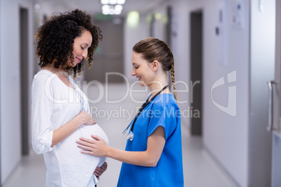 Doctor touching pregnant womans belly in corridor