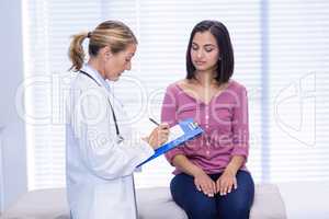 Doctor interacting with patient while writing on clipboard