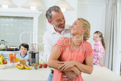 Couple embracing each other while kids smiling in background