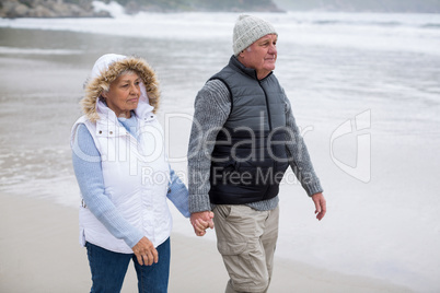 Senior couple walking toward the ocean while holding hands