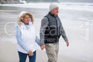 Senior couple walking toward the ocean while holding hands