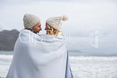 Mature couple wrapped in blanket on the beach