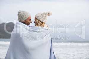 Mature couple wrapped in blanket on the beach