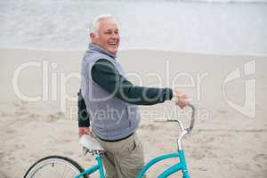 Senior man standing with bicycle on the beach