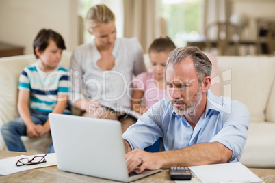 Man using laptop with bills on table in living room