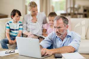 Man using laptop with bills on table in living room