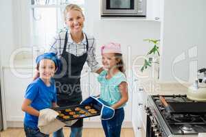 Mother and kids holding tray of baked cookies in kitchen
