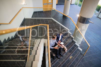 Businessman and woman sitting on steps using laptop and digital tablet