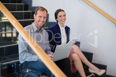 Businessman and woman sitting on steps holding laptop