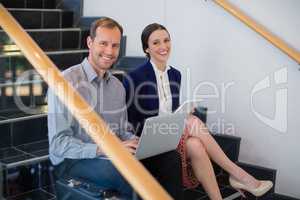 Businessman and woman sitting on steps holding laptop