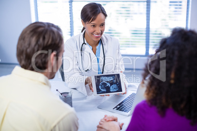Couple looking at babies ultrasound scan on doctors digital tablet