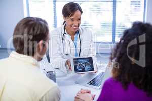 Couple looking at babies ultrasound scan on doctors digital tablet