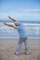 Senior man doing stretching exercise on the beach