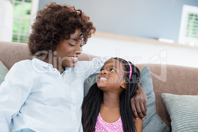 Mother and daughter interacting while sitting on sofa in living room