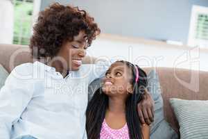 Mother and daughter interacting while sitting on sofa in living room