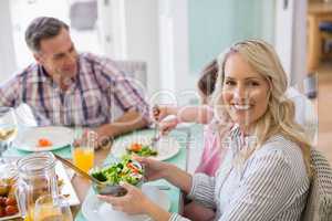 Smiling woman holding bowl of salad on dinning table