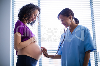 Doctor examining pregnant womans belly with stethoscope in ward