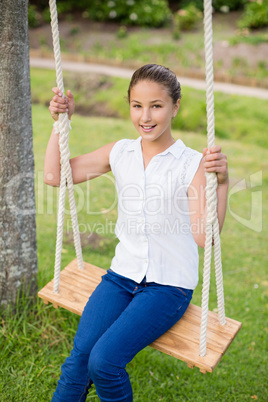 Happy girl sitting on a swing in park