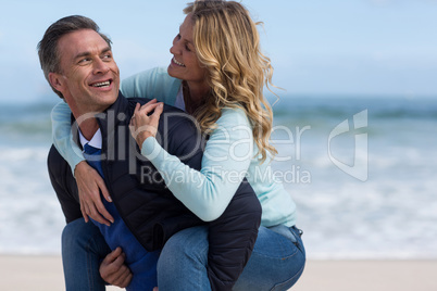 Mature man giving piggyback ride to woman on beach
