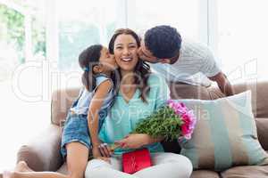 Woman receiving kiss from his husband and daughter in living room