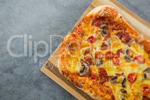 Pizza served in a chopping board on a wooden plank