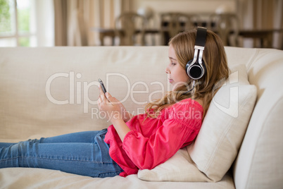 Cute girl lying on sofa and listening to music on headphones in living room