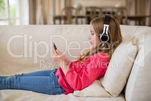 Cute girl lying on sofa and listening to music on headphones in living room