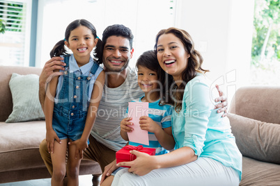 Portrait of parents and kids sitting on sofa with present in living room