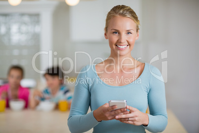 Happy beautiful woman using mobile phone in kitchen