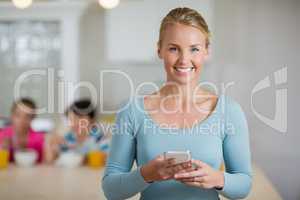 Happy beautiful woman using mobile phone in kitchen