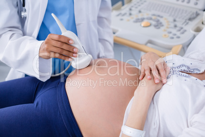 Mid section of doctor doing ultrasound scan for pregnant woman