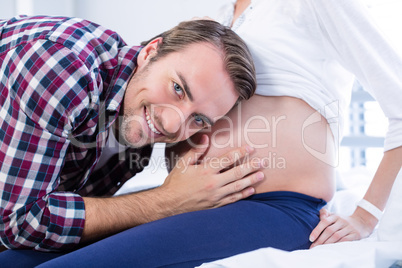 Smiling man listening to pregnant womans belly in ward