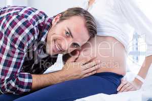 Smiling man listening to pregnant womans belly in ward