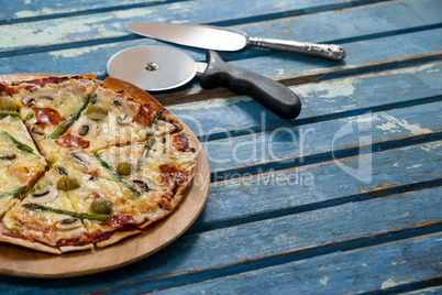 Delicious pizza served on pizza tray with cutter and knife on wooden plank