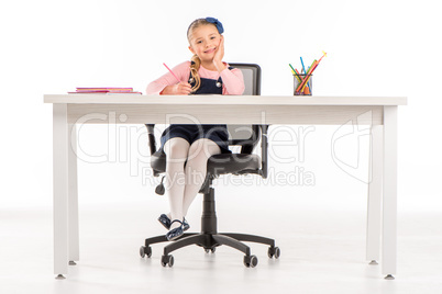 Smiling schoolgirl sitting at desk with books