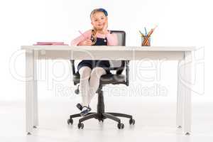 Smiling schoolgirl sitting at desk with books