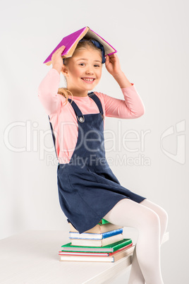 Smiling schoolgirl sitting on books