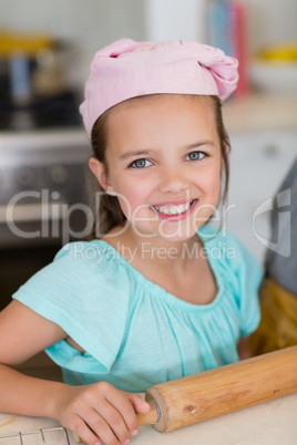 Smiling girl wearing chefs hat with rolling pin in kitchen at home