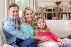 Portrait of parents and daughter sitting on sofa in living room
