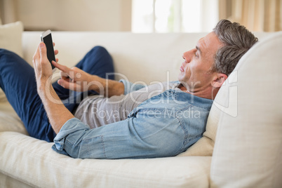 Man lying on sofa and using mobile phone in living room