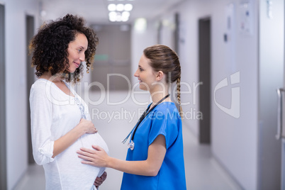 Doctor touching pregnant womans belly in corridor