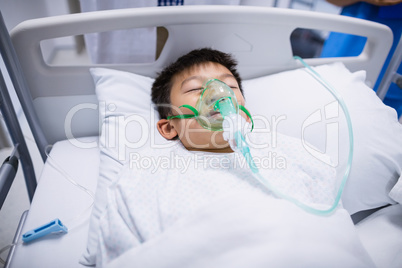 Boy patient wearing oxygen mask lying on hospital bed